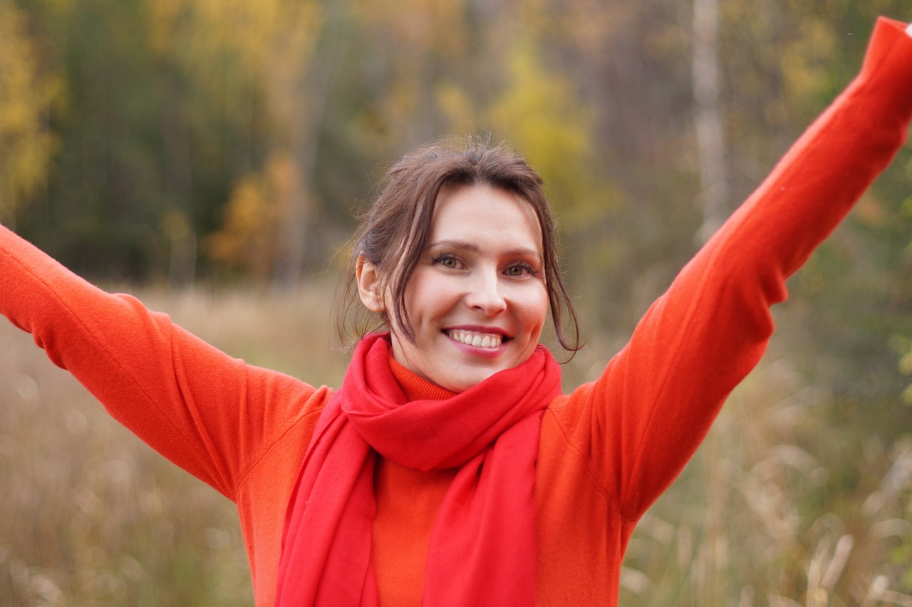 Young woman in red top and scarf smiling with arms held aloft in the air
