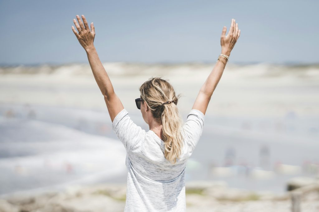 of a woman at the beach with her hands above her head. Photo by Guillaume de Germain.