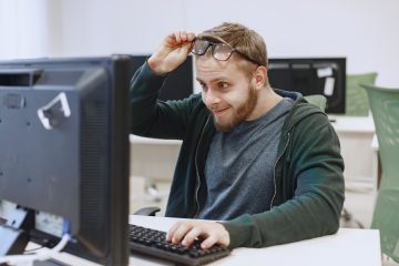Young man looking at a computer sccreen and taking his glasses off to see better