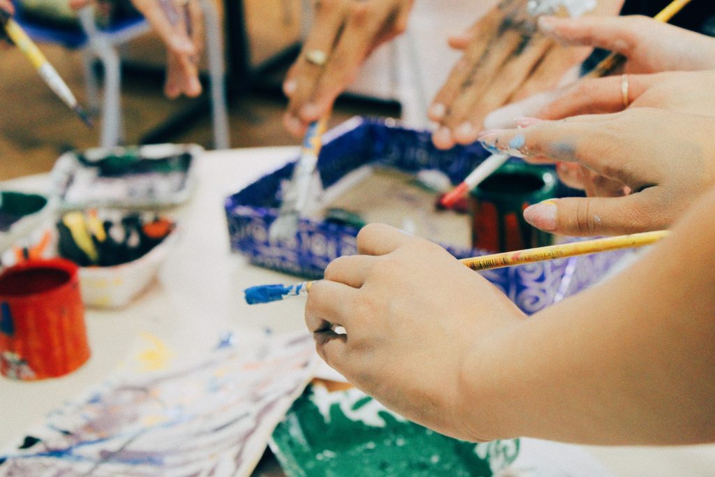 Hands of different people with paint and paint brushes.