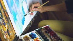 A hand painting a picture with some colours beside