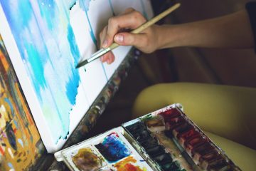 A hand painting a picture with some colours beside