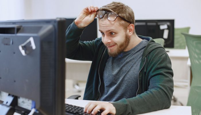 Young man looking at a computer sccreen and taking his glasses off to see better