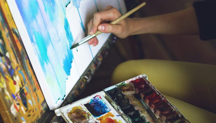 A hand painting a picture with some colours beside